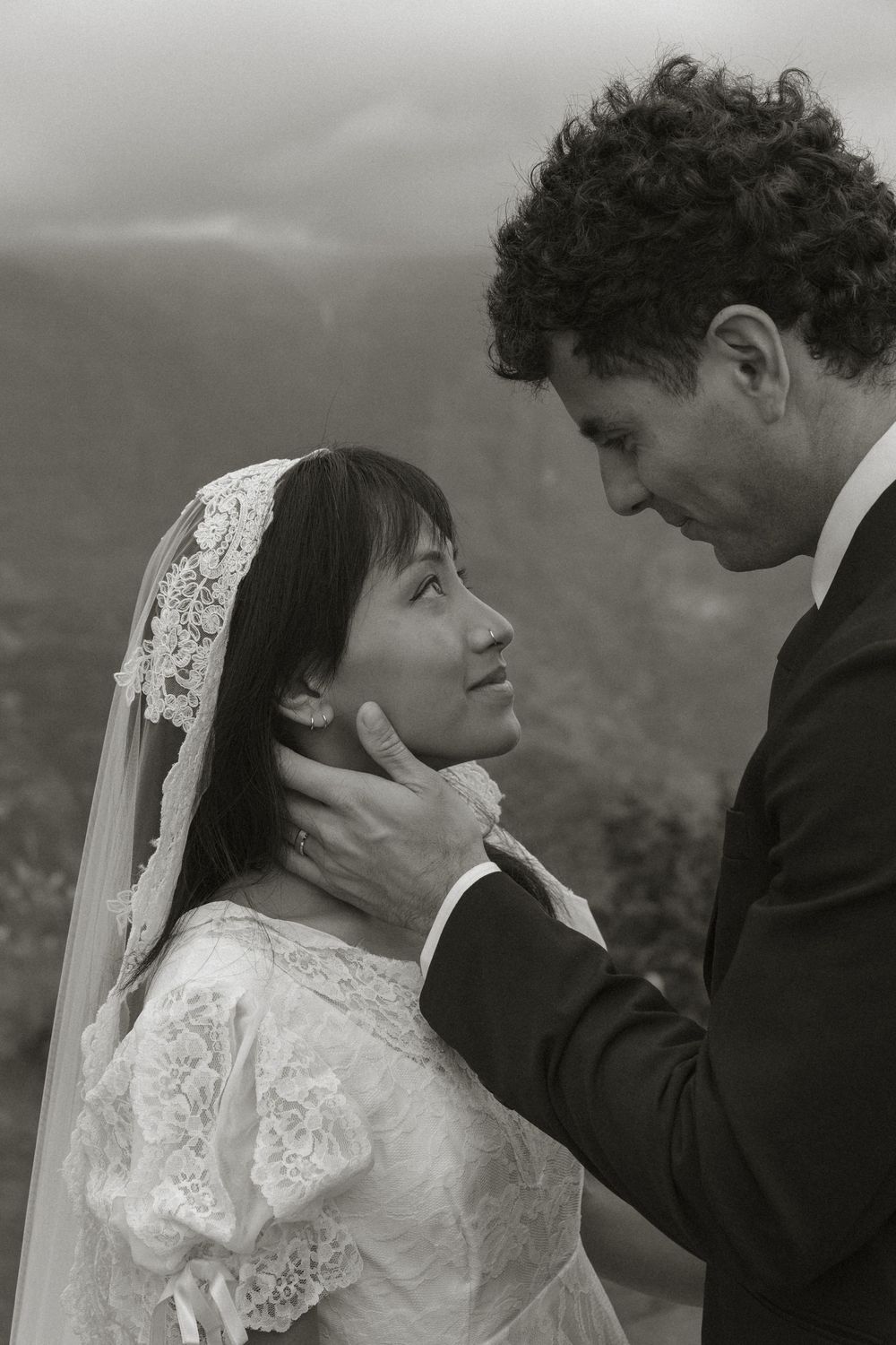 A romantic moment between newlyweds against a misty mountain backdrop in black and white.