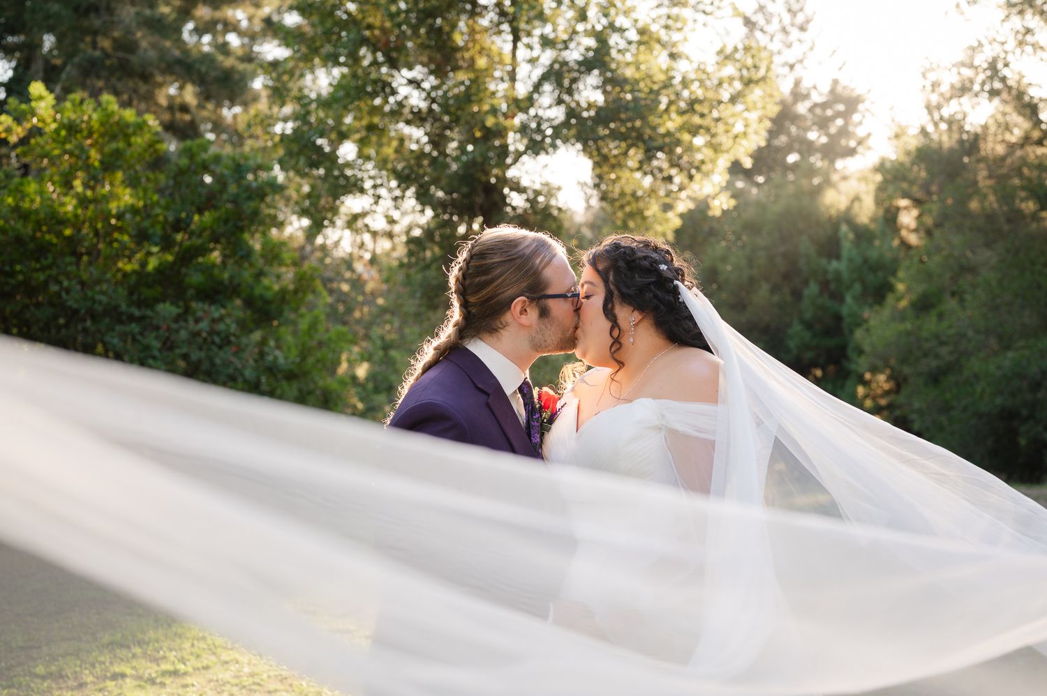 Couple in formal wedding attire walking along scenic mountain path during golden sunset.