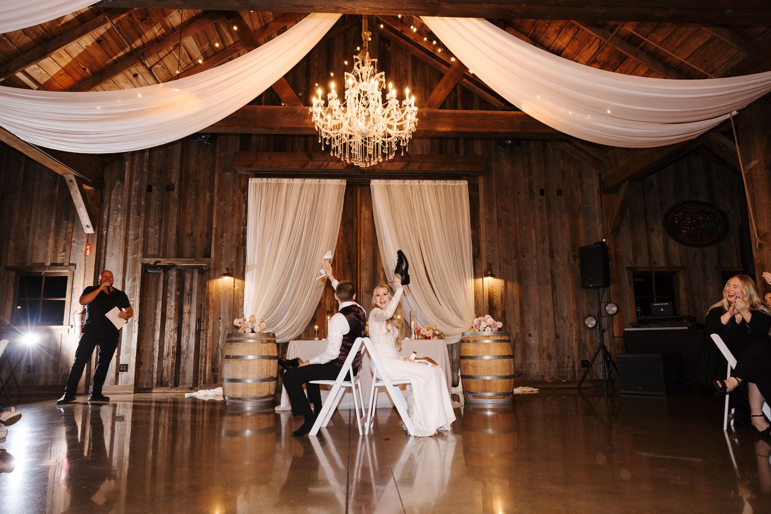 Elegant barn wedding venue decorated with white drapes and crystal chandeliers showing multiple dance moments.