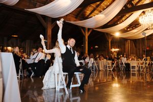 Wedding reception guests dance and celebrate on a rustic wooden dance floor under romantic string lights at an evening venue.