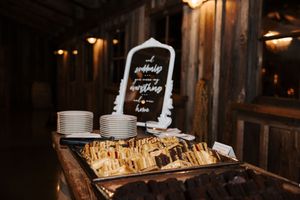 Rustic wedding reception setup with sandwich platters and white plates on wooden tables.