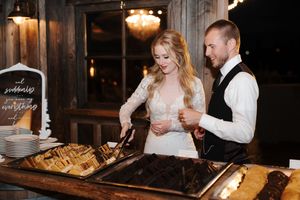 A couple in wedding attire shares an intimate moment while cutting their wedding cake at a rustic venue.