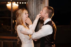 A couple in wedding attire playfully feed each other cake during their reception in a dimly lit venue.
