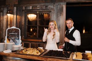 A newlywed couple slices into their wedding cake together at a dimly lit rustic reception venue.