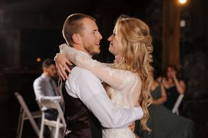 A couple shares their first dance at an outdoor evening wedding reception while guests watch from folding chairs.