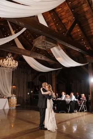 Elegant barn wedding reception venue with white draping, crystal chandeliers and rustic wooden beams.