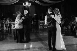 Black and white wedding reception dance floor scene with couples dancing under a chandelier.
