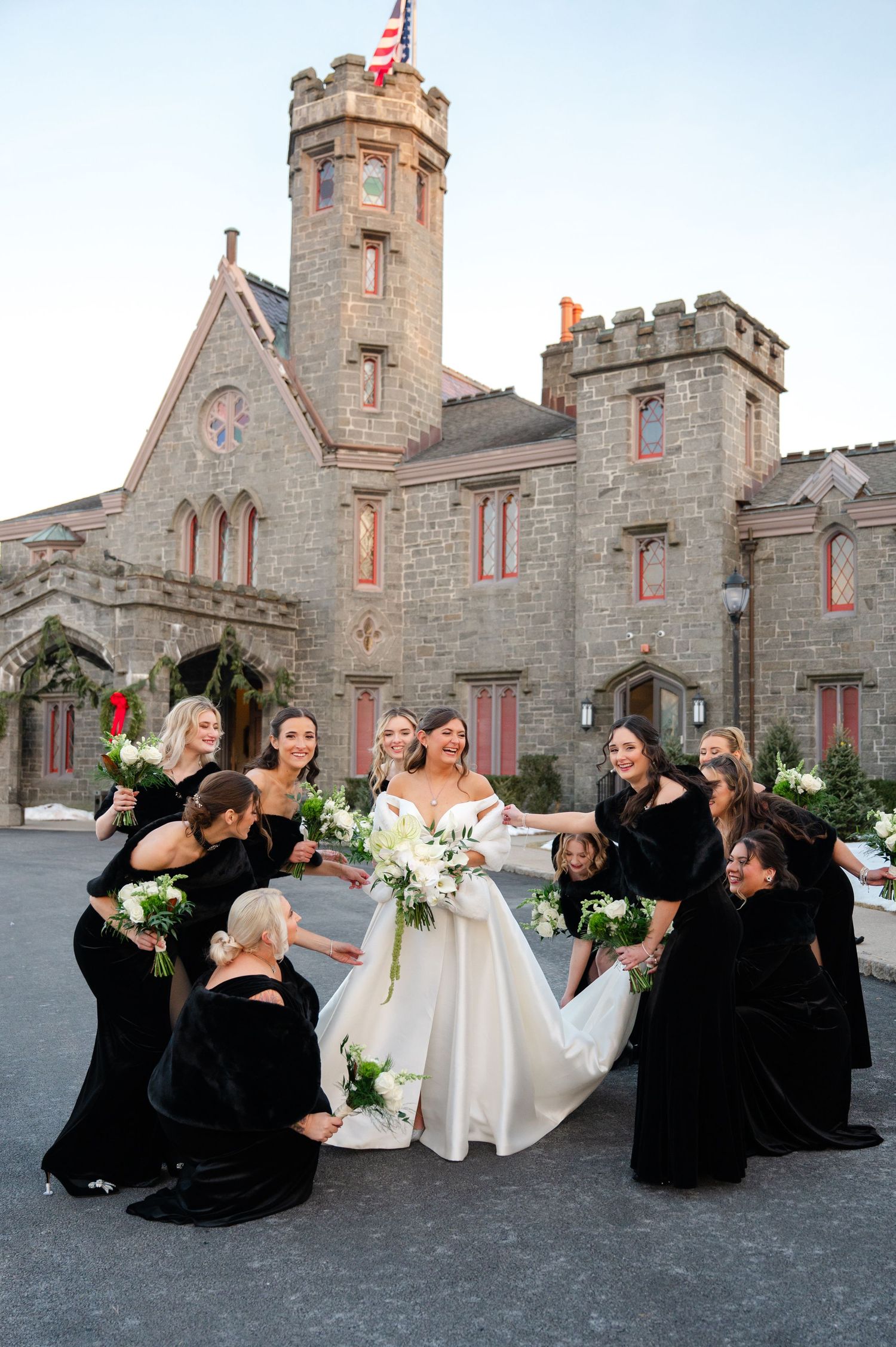 A bride laughs as she is attended to by her bridesmaids outside of the historic Whitby Castle wedding venue in Rye, NY.