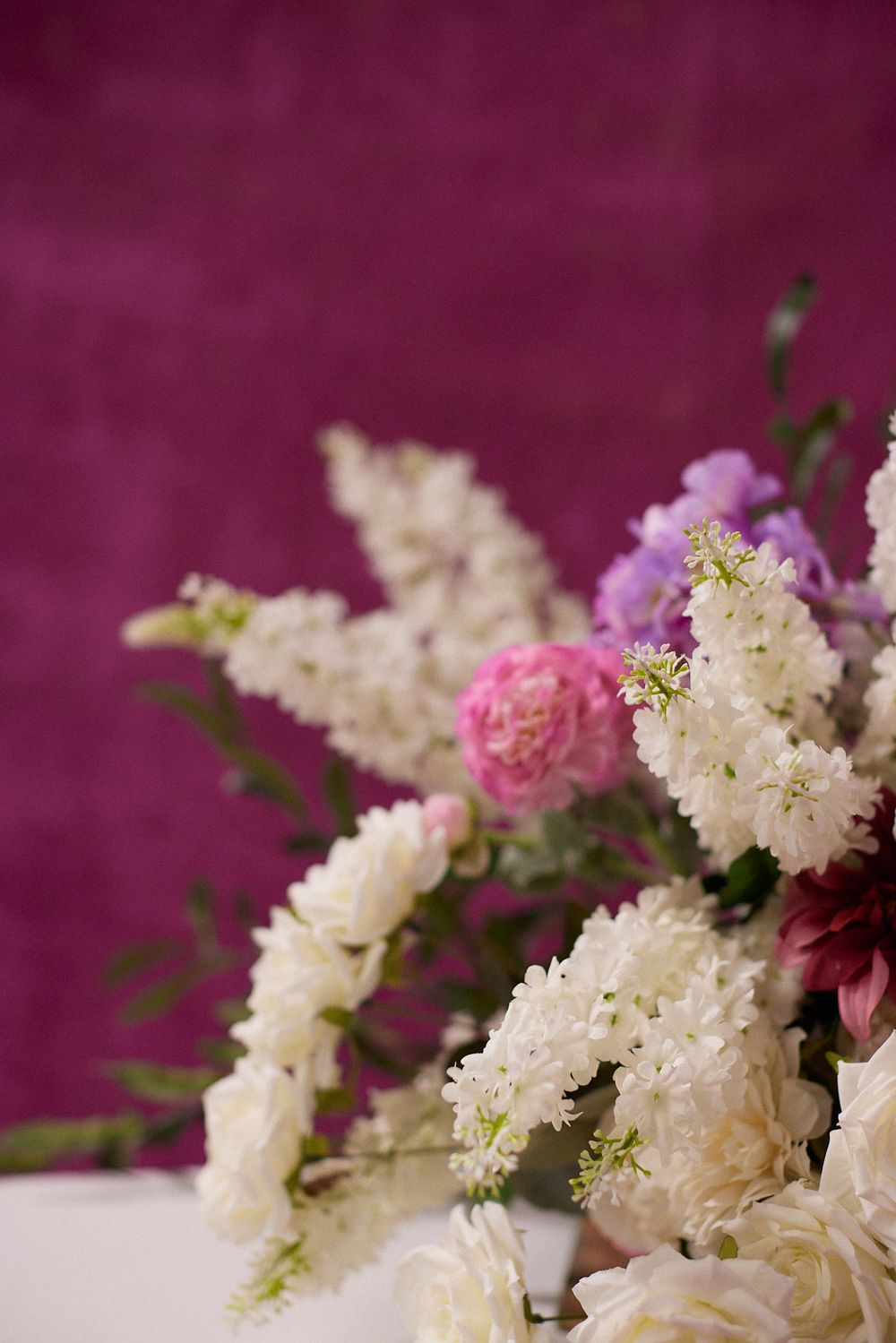 A beautiful floral arrangement with white stock flowers, pink carnations, and purple blooms against a rich magenta background.