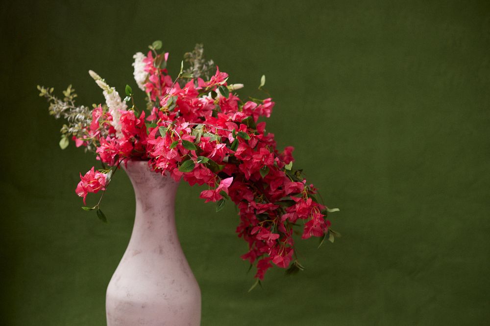 Pink vase with vibrant red and pink flowers against a dark green background.