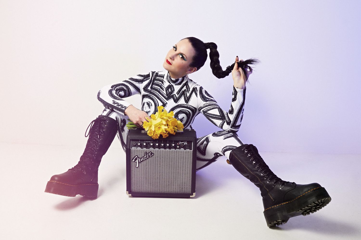 Woman in black and white outfit with pigtails poses with a Fender amp and yellow flowers wearing purple combat boots.