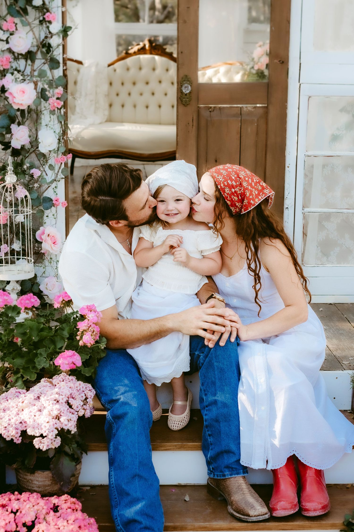 Sweet family moment captured on a porch with pink flowers and white decor in a rustic country setting.