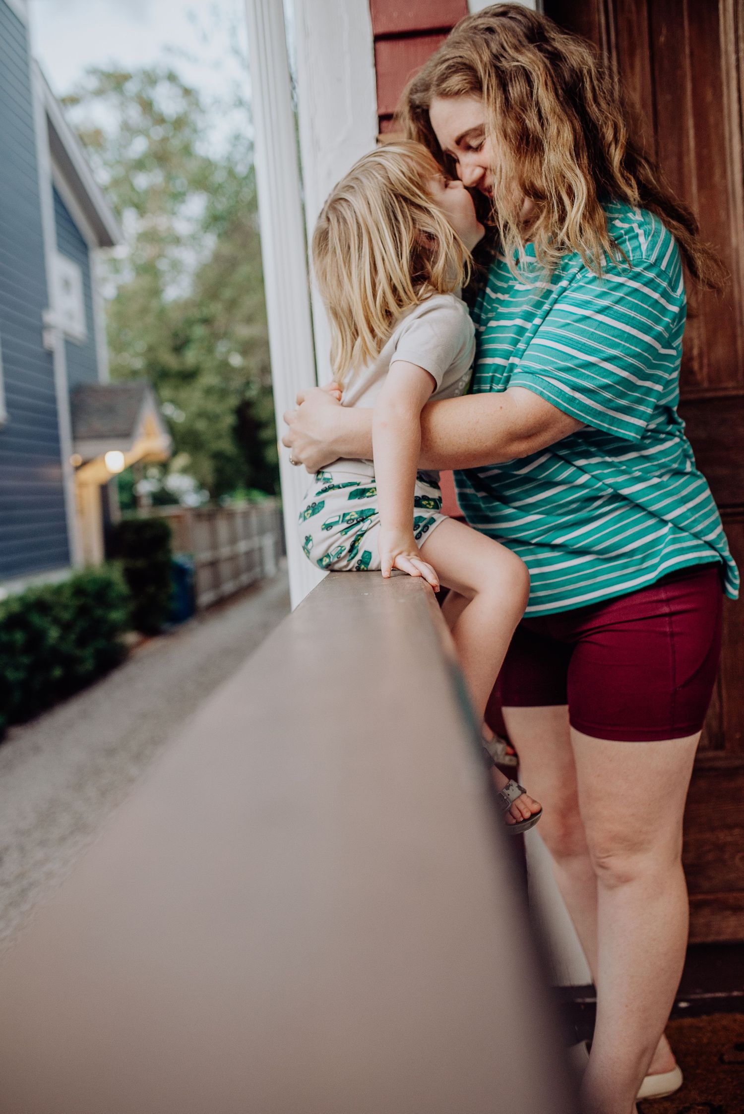 A parent and child wearing matching green striped shirts embrace on a front porch during a tender moment.