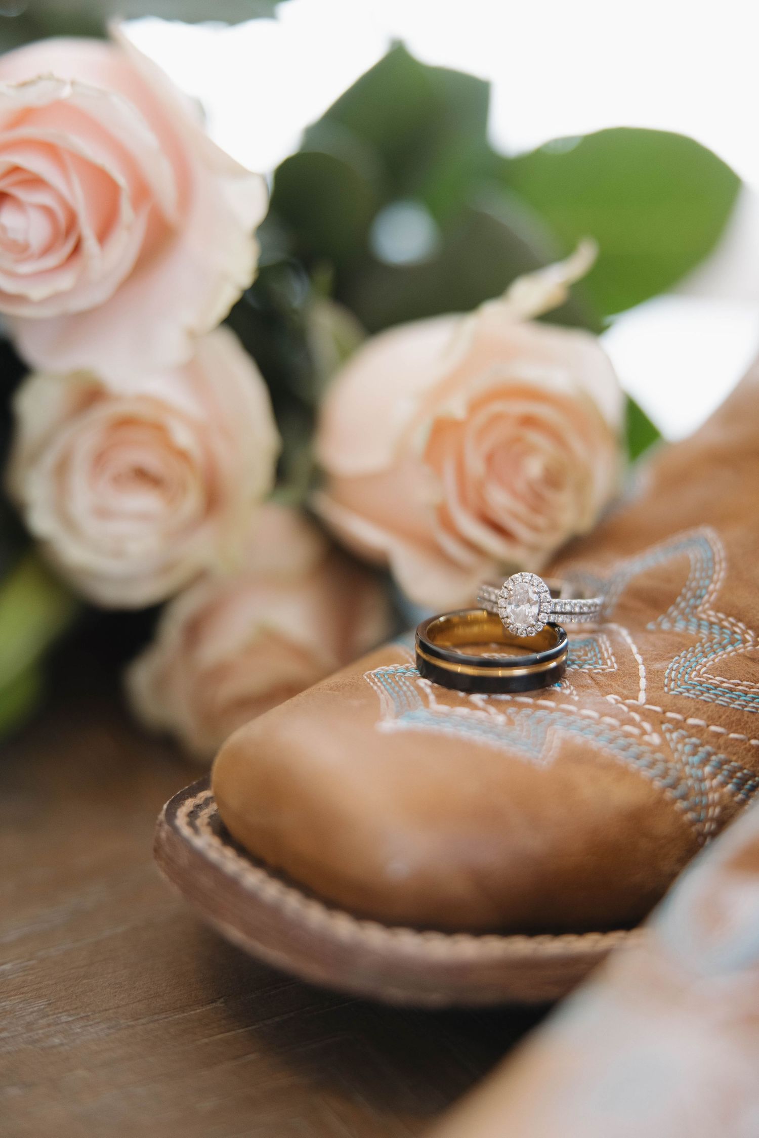 Wedding rings and engagement ring displayed on pink ballet shoes with soft roses in the background.