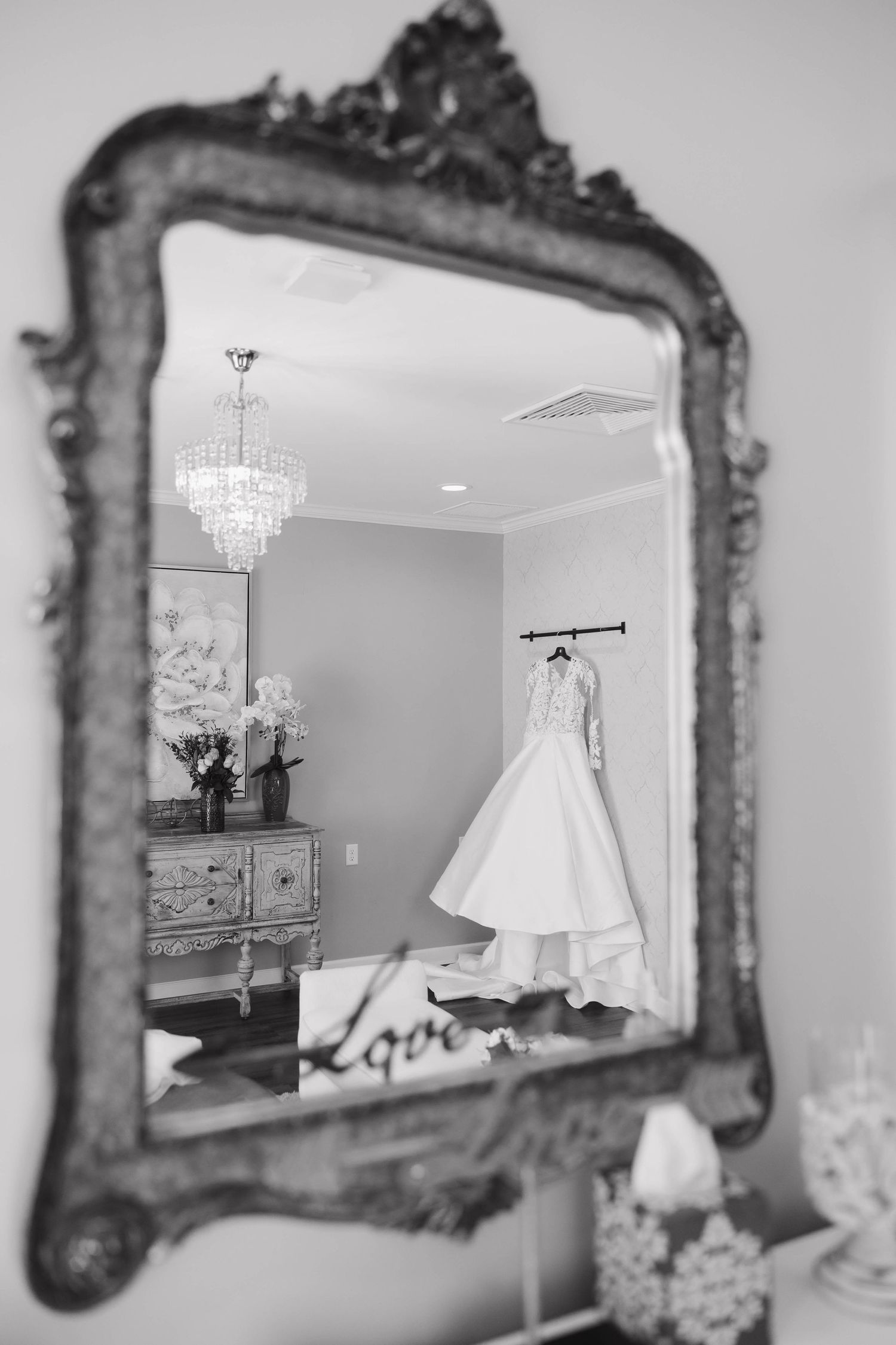 Elegant wedding dress hangs in a room with ornate vintage mirrors and crystal chandelier lighting.