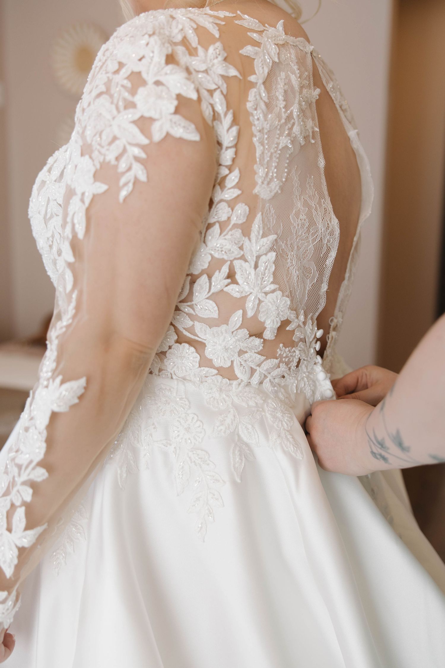 Close-up detail of delicate floral lace appliques on a white wedding dress bodice with sheer sleeves.