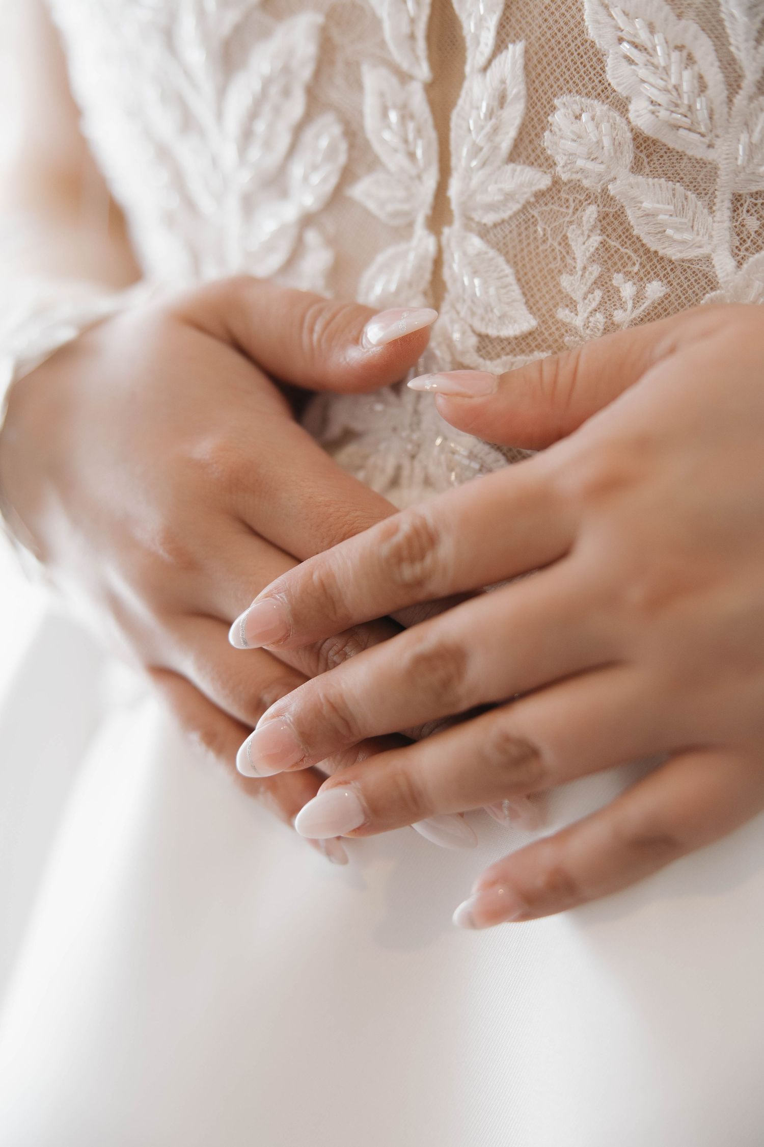 Elegant hands with manicured nails against intricate white lace wedding dress detail.