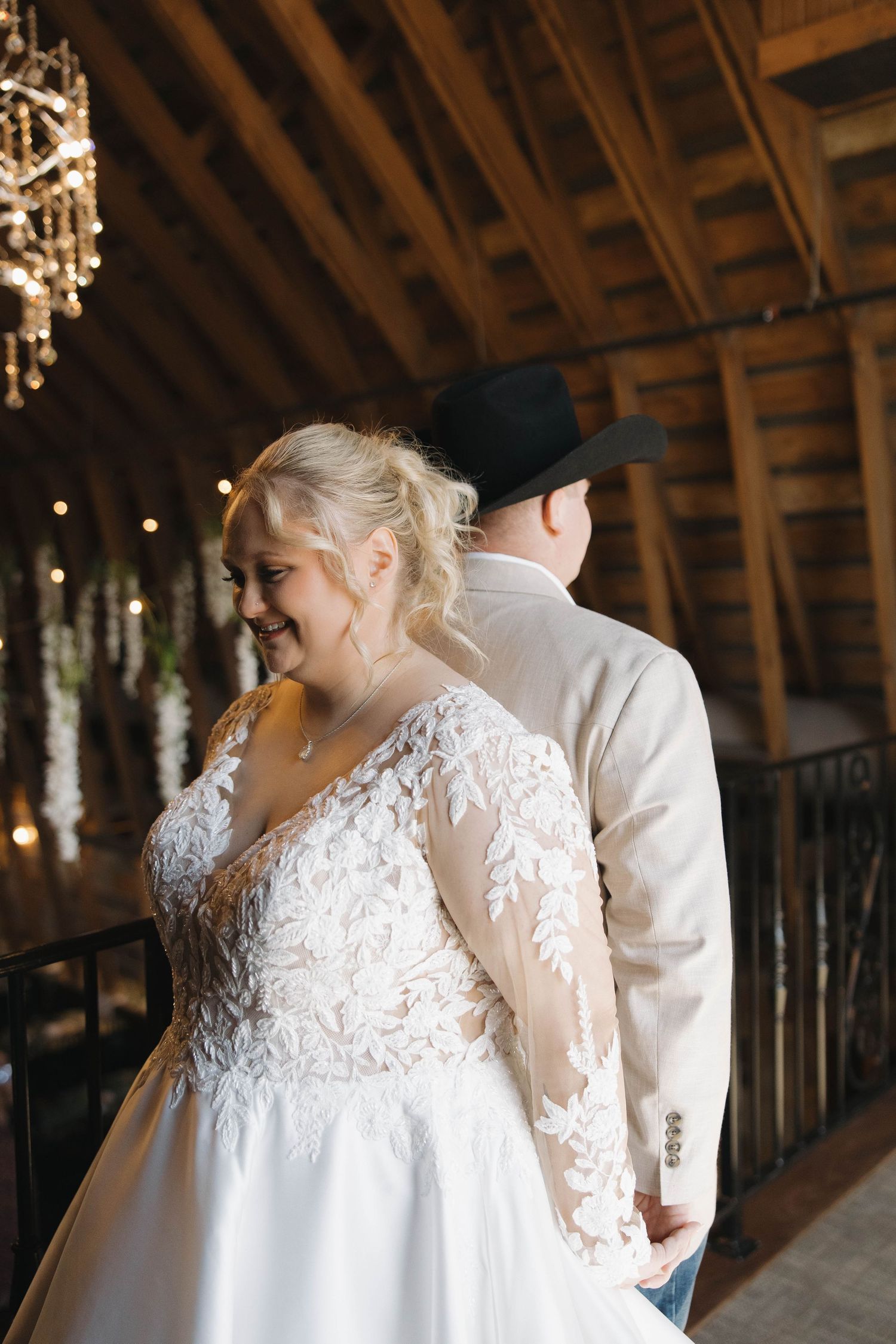 A romantic wedding scene in a rustic barn venue with crystal chandelier lighting.