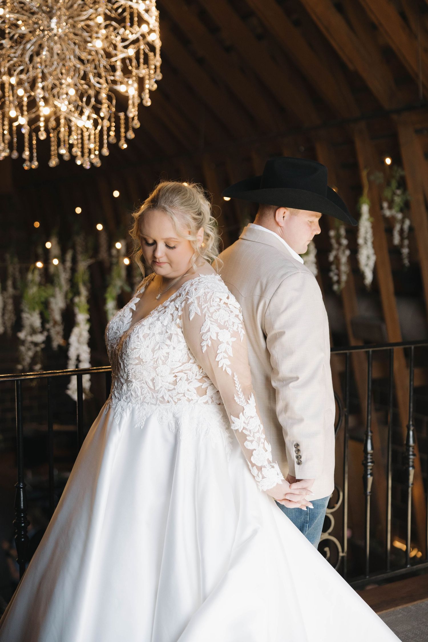 Wedding couple dancing under crystal chandeliers in a rustic barn venue with romantic lighting.