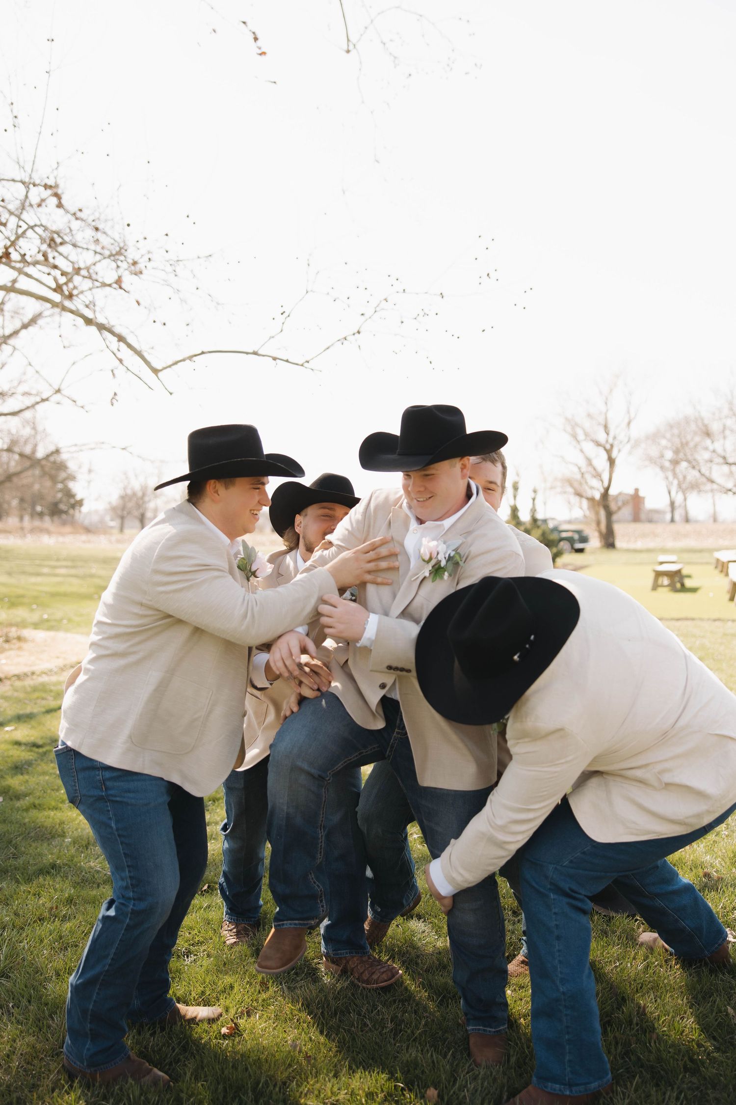 Playful groomsmen in cowboy hats and jeans posing in sequence on a sunny field.