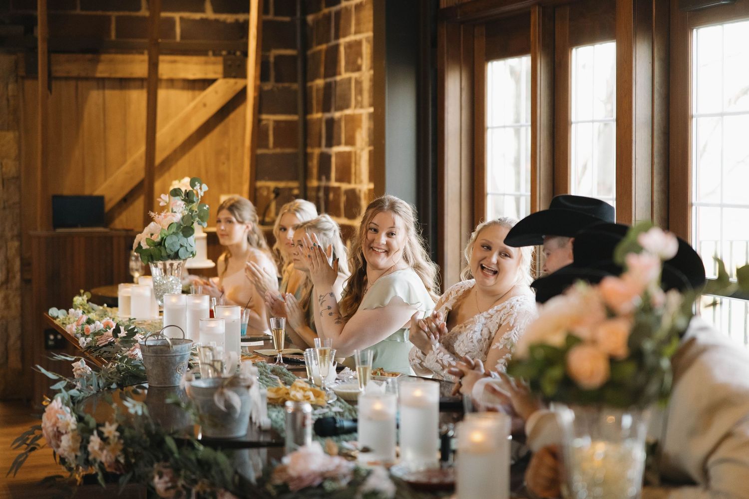 Wedding reception table decorated with floral centerpieces and candles in rustic brick venue.