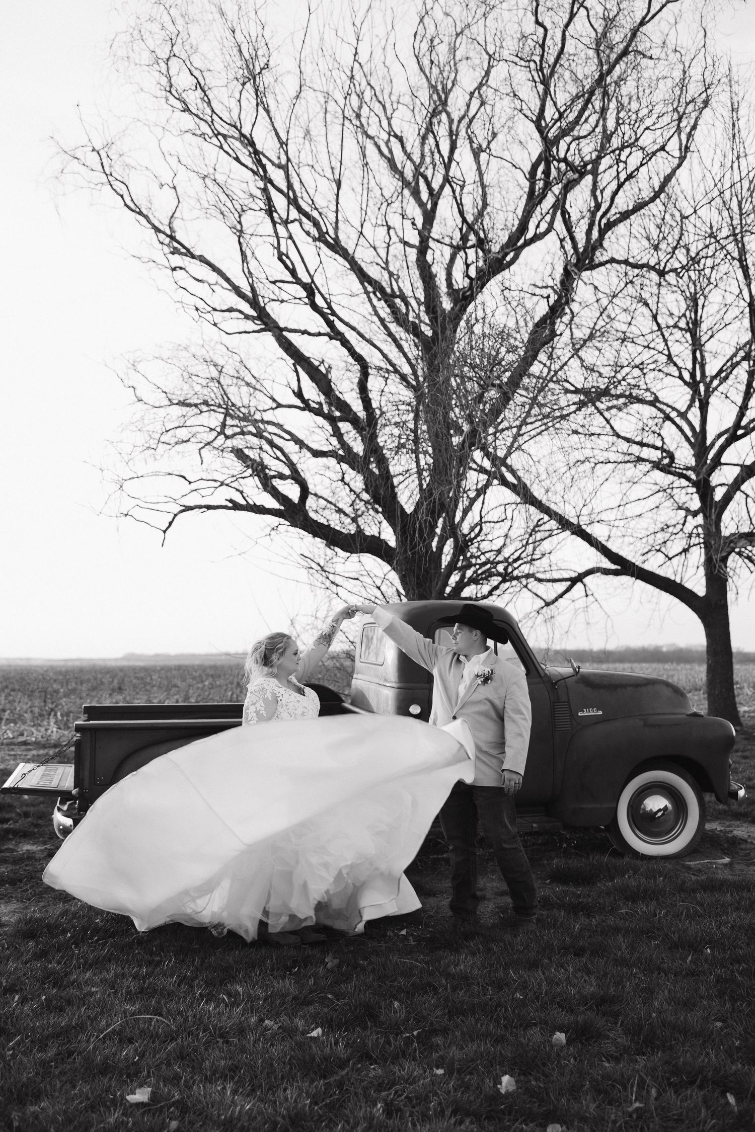 Black and white wedding photo sequence with vintage truck and flowing dress in countryside setting.