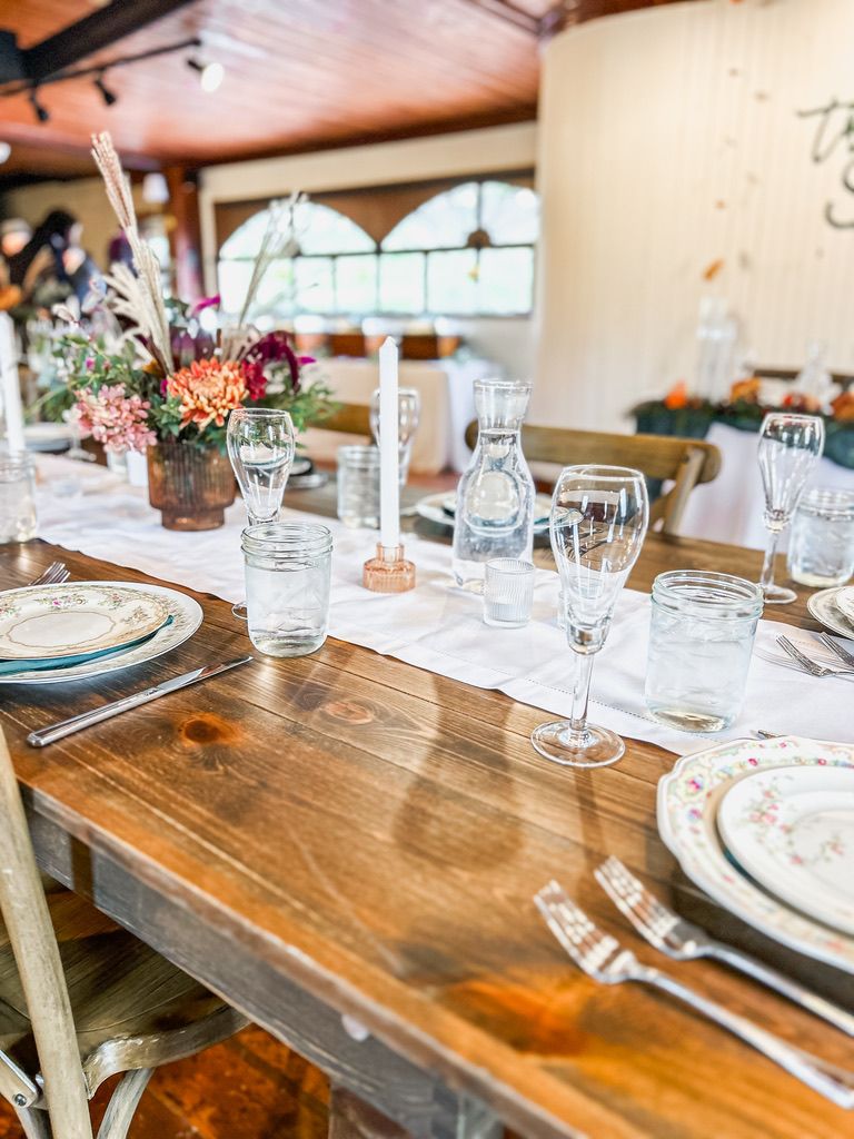 Elegant rustic wedding reception table set with glassware, floral centerpieces, candles, and vintage mismatched china plates.