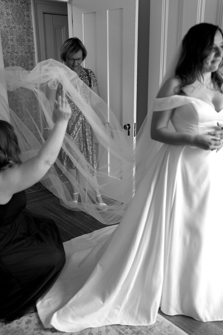Black and white photo of bride being helped into veil by bridesmaids in elegant bridal suite.