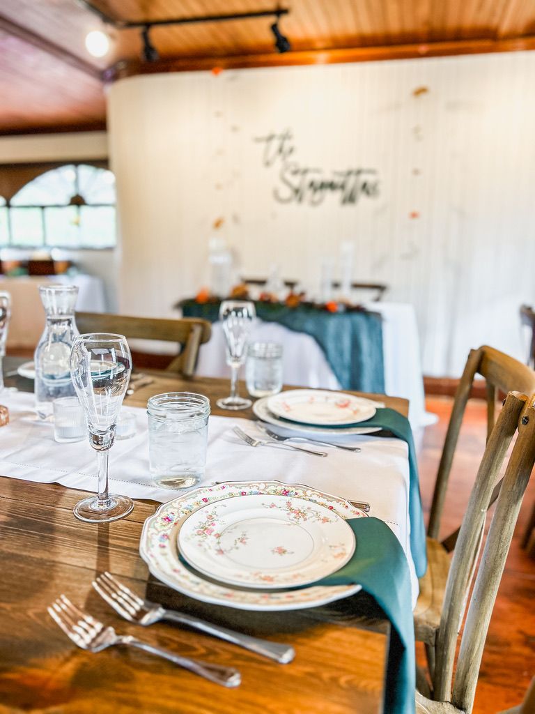 Elegantly set dining table with teal runner, vintage china, and glassware in a rustic venue.