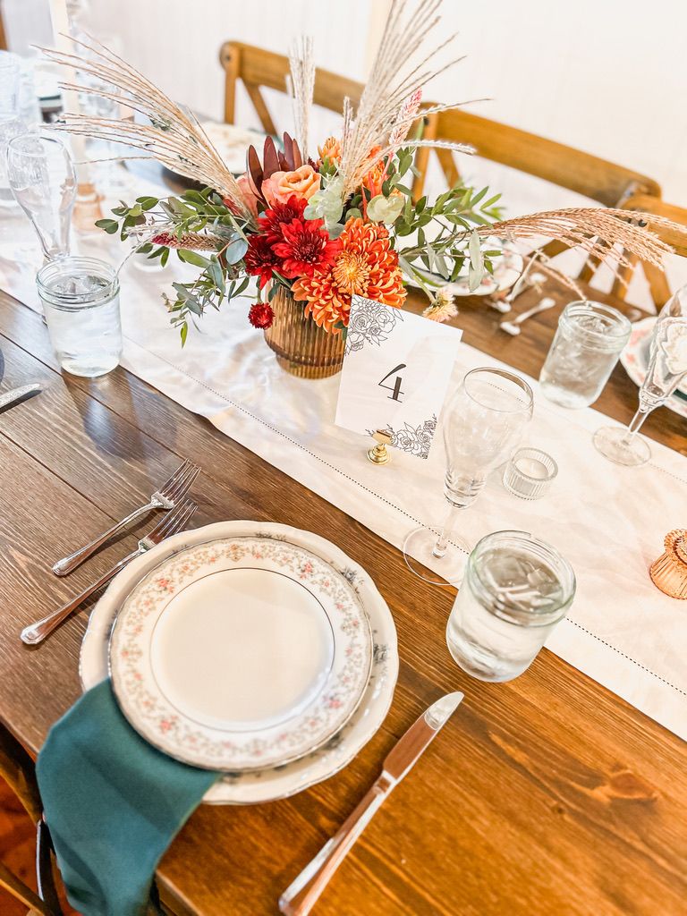 Rustic wooden wedding reception table with floral centerpiece, teal napkins, vintage china, and table number four.