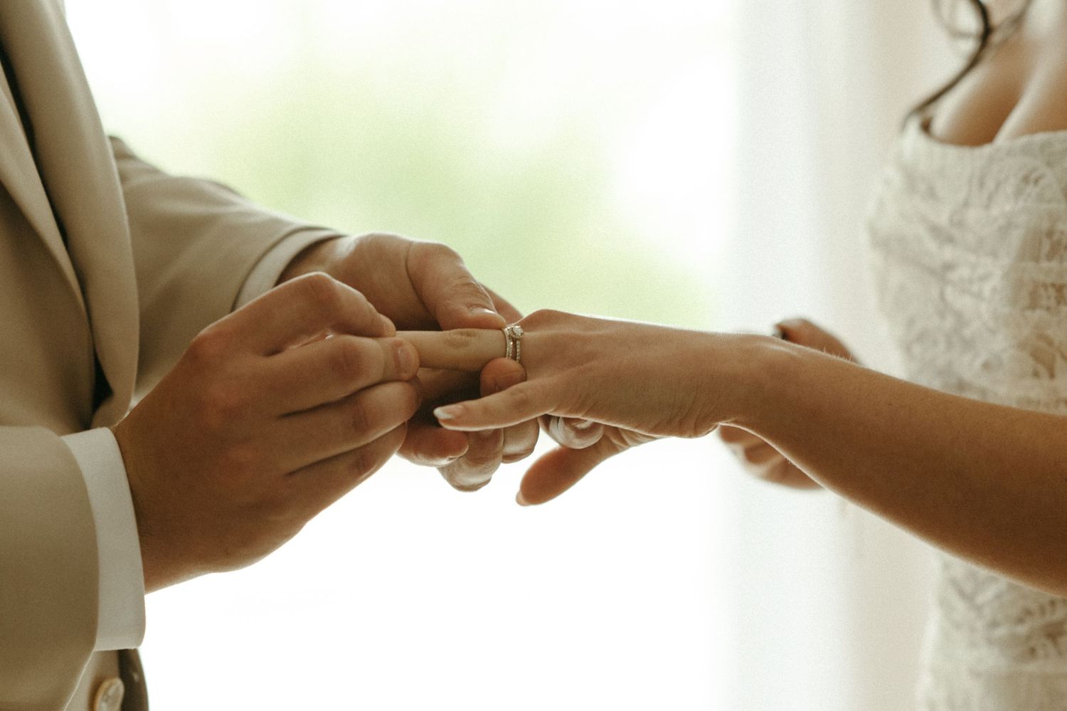 Groom placing wedding ring on bride's finger during intimate outdoor wedding ceremony.