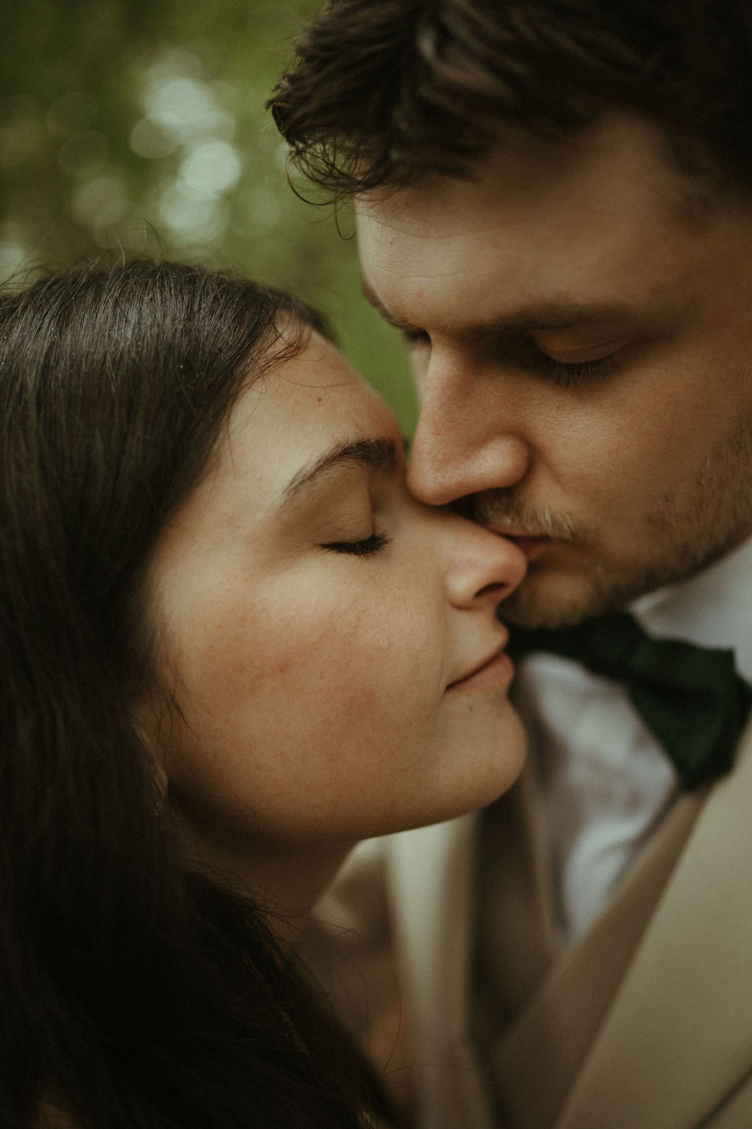 Close-up of groom tenderly kissing bride on forehead, both with eyes closed in romantic moment.