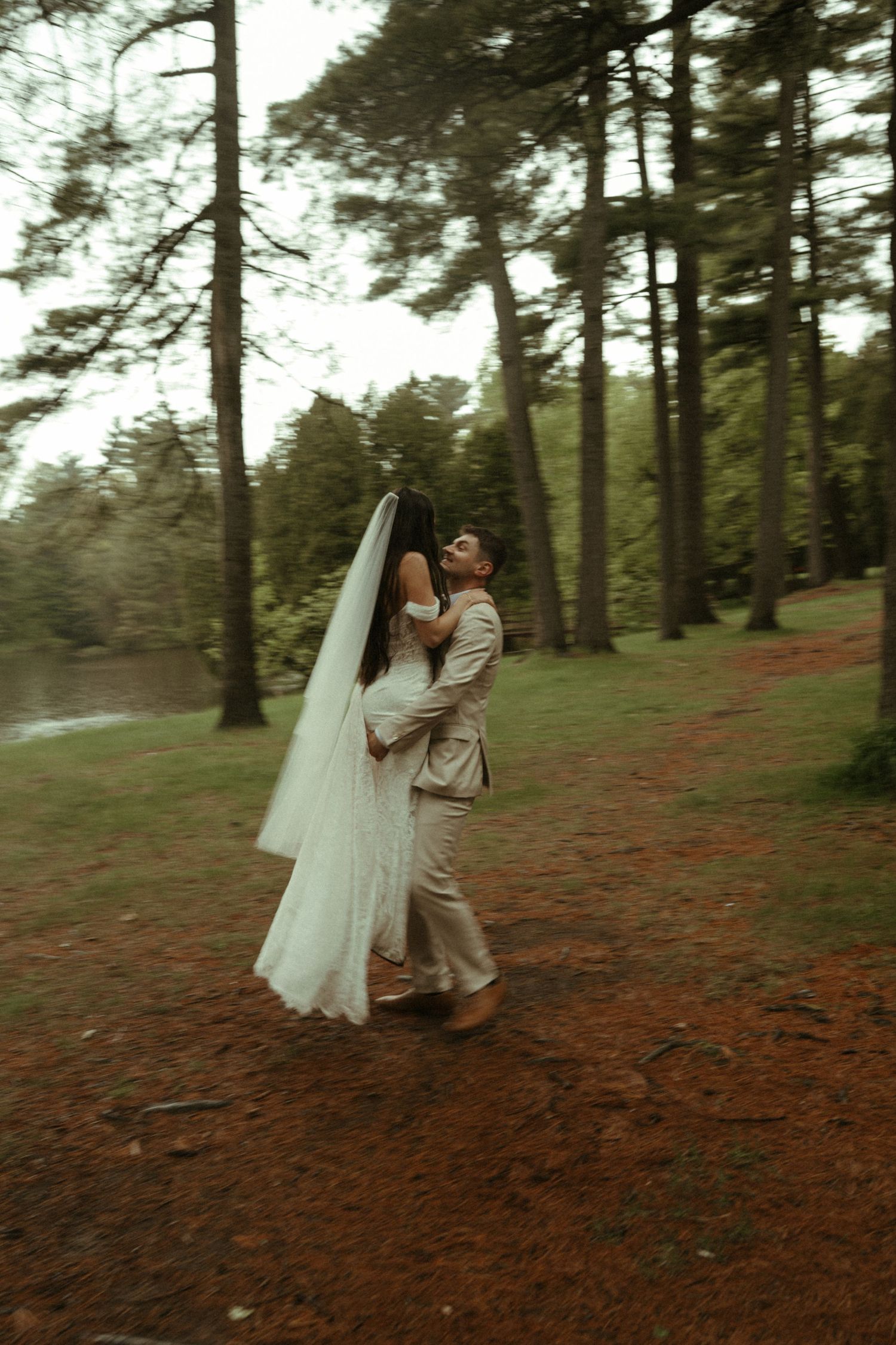 Bride and groom embrace in a lush forest setting, her white veil flowing as they share a romantic wedding moment.