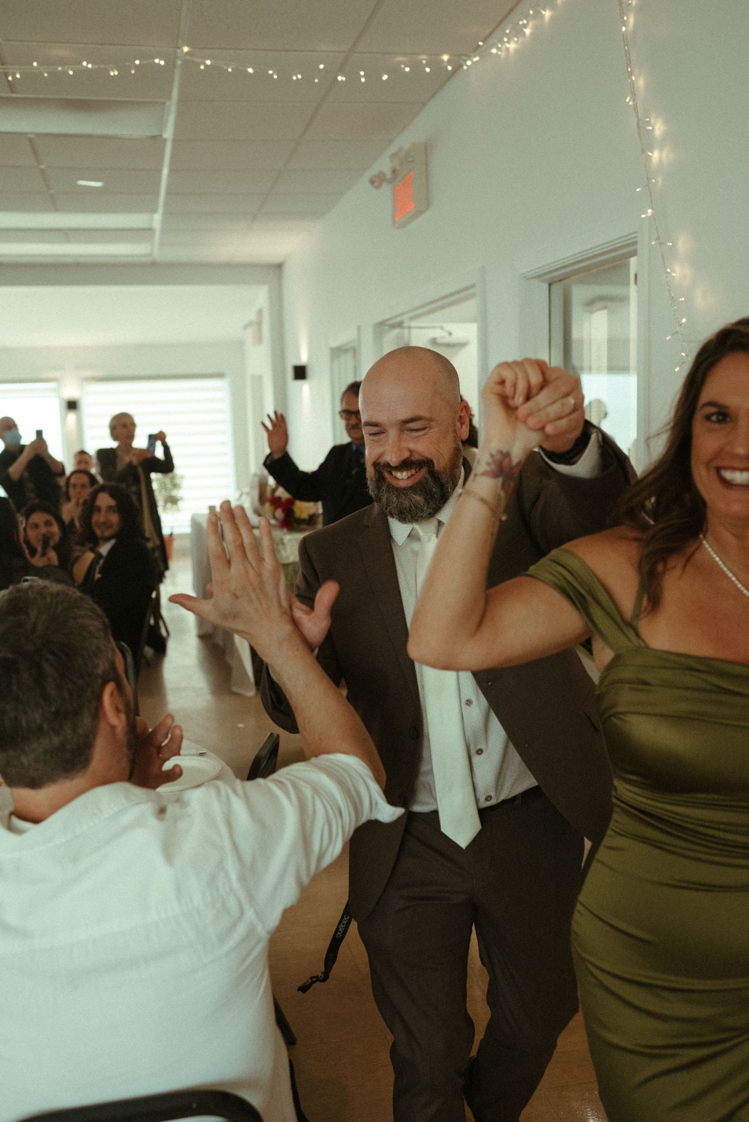 Groom in gray suit celebrates with guests during lively wedding reception entrance dance.