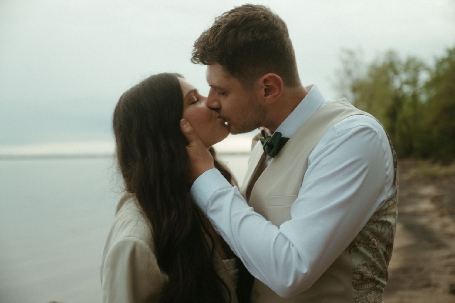 Bride and groom sharing romantic kiss near waterfront on their wedding day.