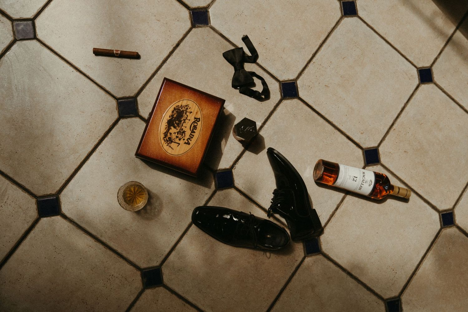 An assortment of personal items, including a book, glasses, and a bottle, on a tiled floor.