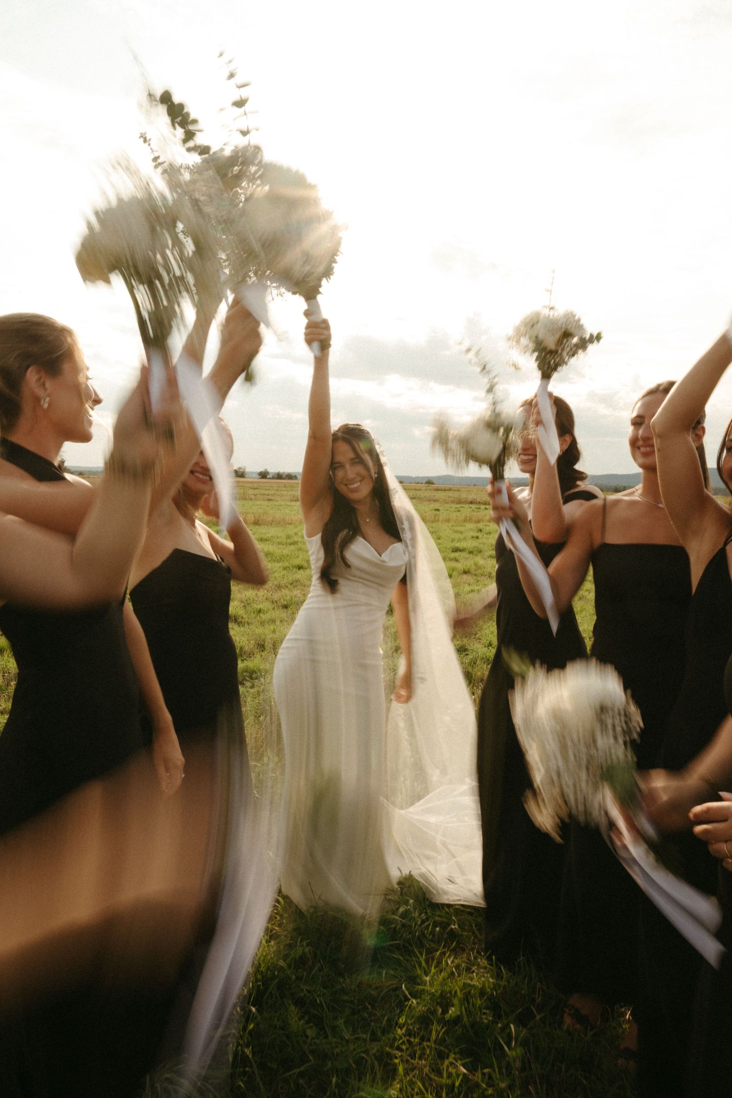 A bride and her bridesmaids tossing bouquets of flowers in a field.