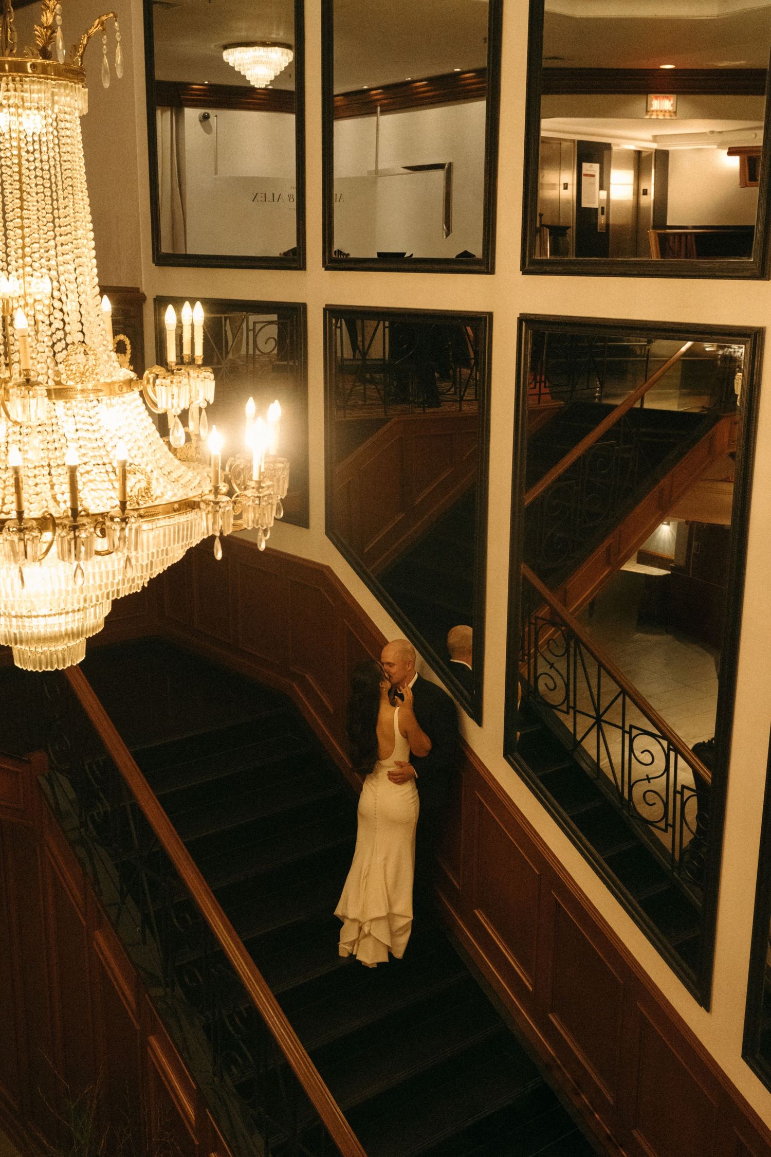A dimly lit hallway with a grand chandelier and ornate mirrors reflecting the warm lighting.