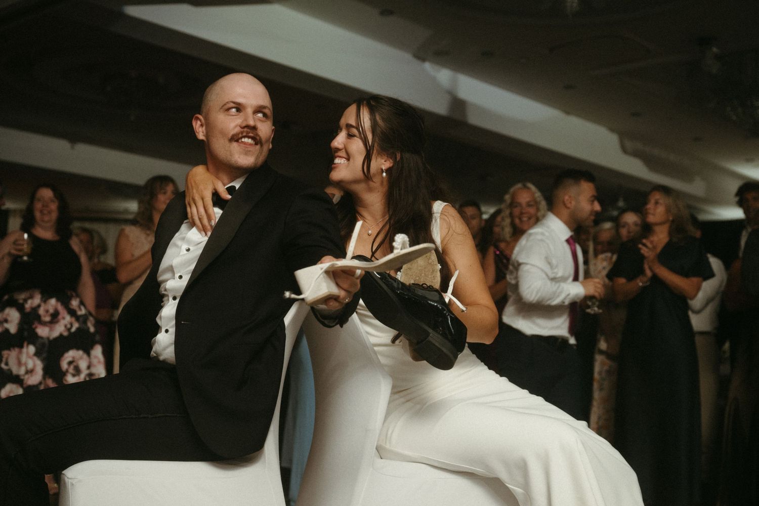 A couple dressed formally are dancing together on a dimly lit dance floor with other people in the background.