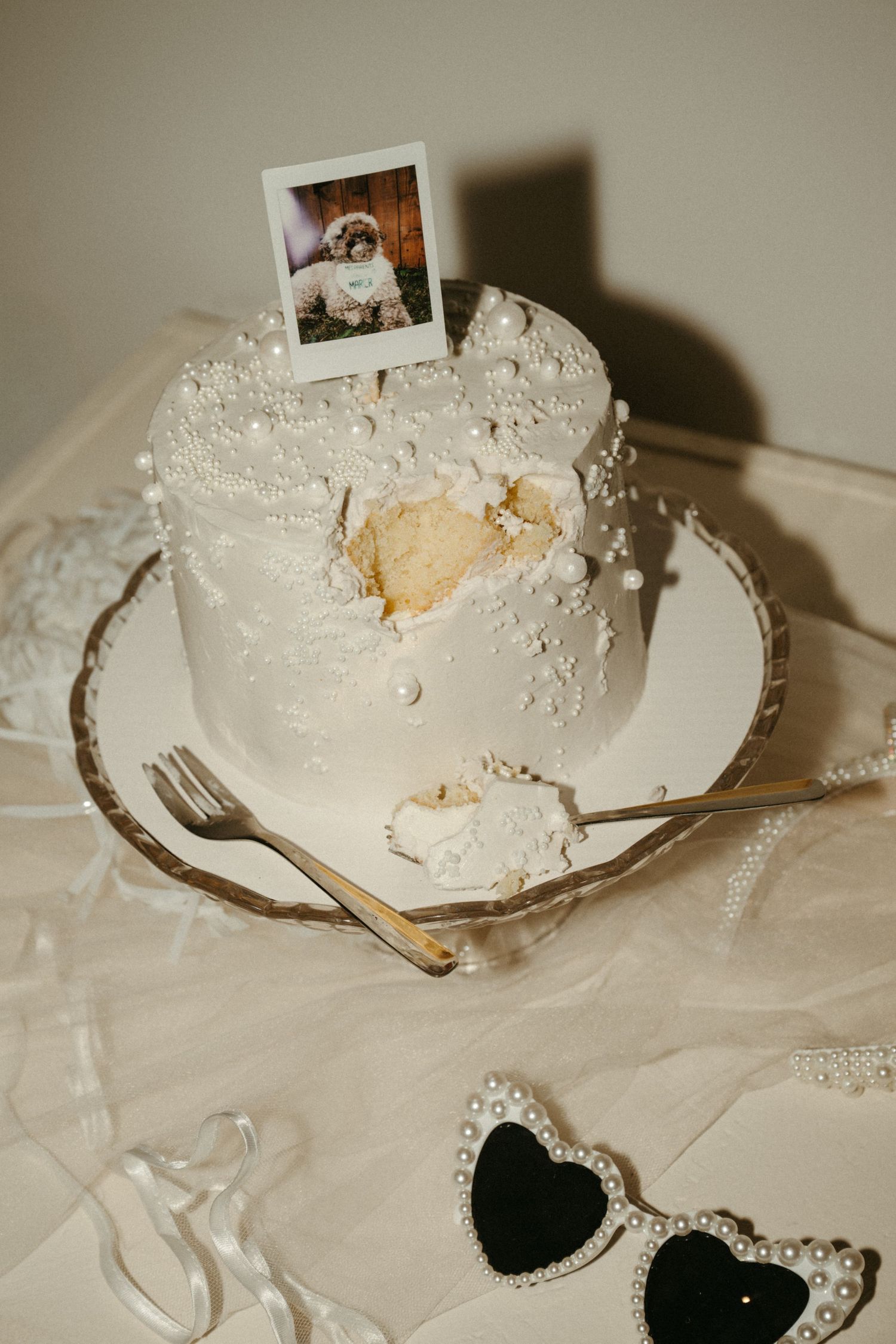 A close-up image of a white wedding cake with a small framed photograph on top.