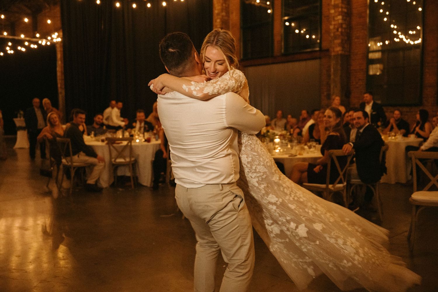 A bride and groom dancing together at their wedding reception, surrounded by lit string lights.