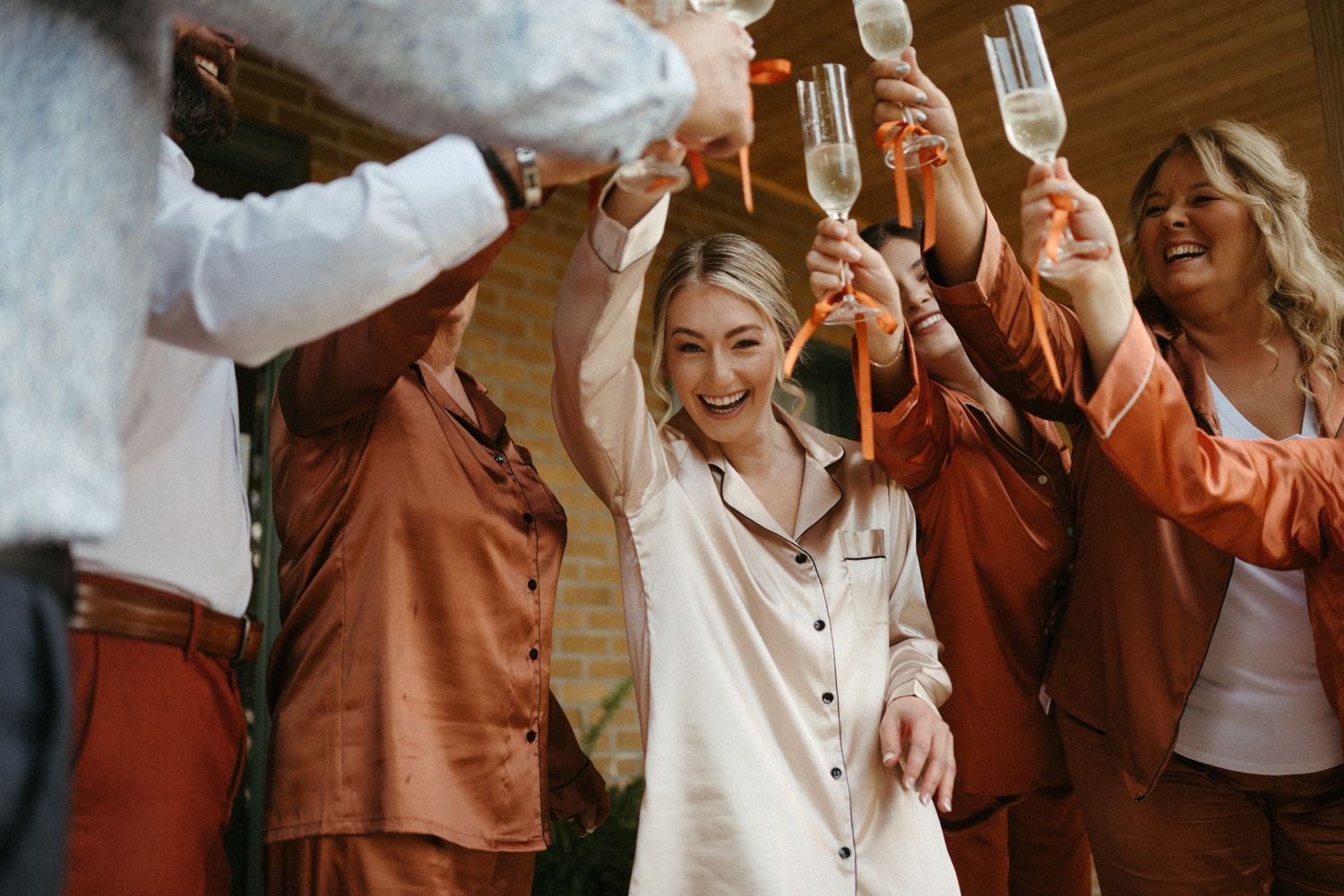 A group of friends celebrating with champagne flutes, dressed in warm-toned outfits.