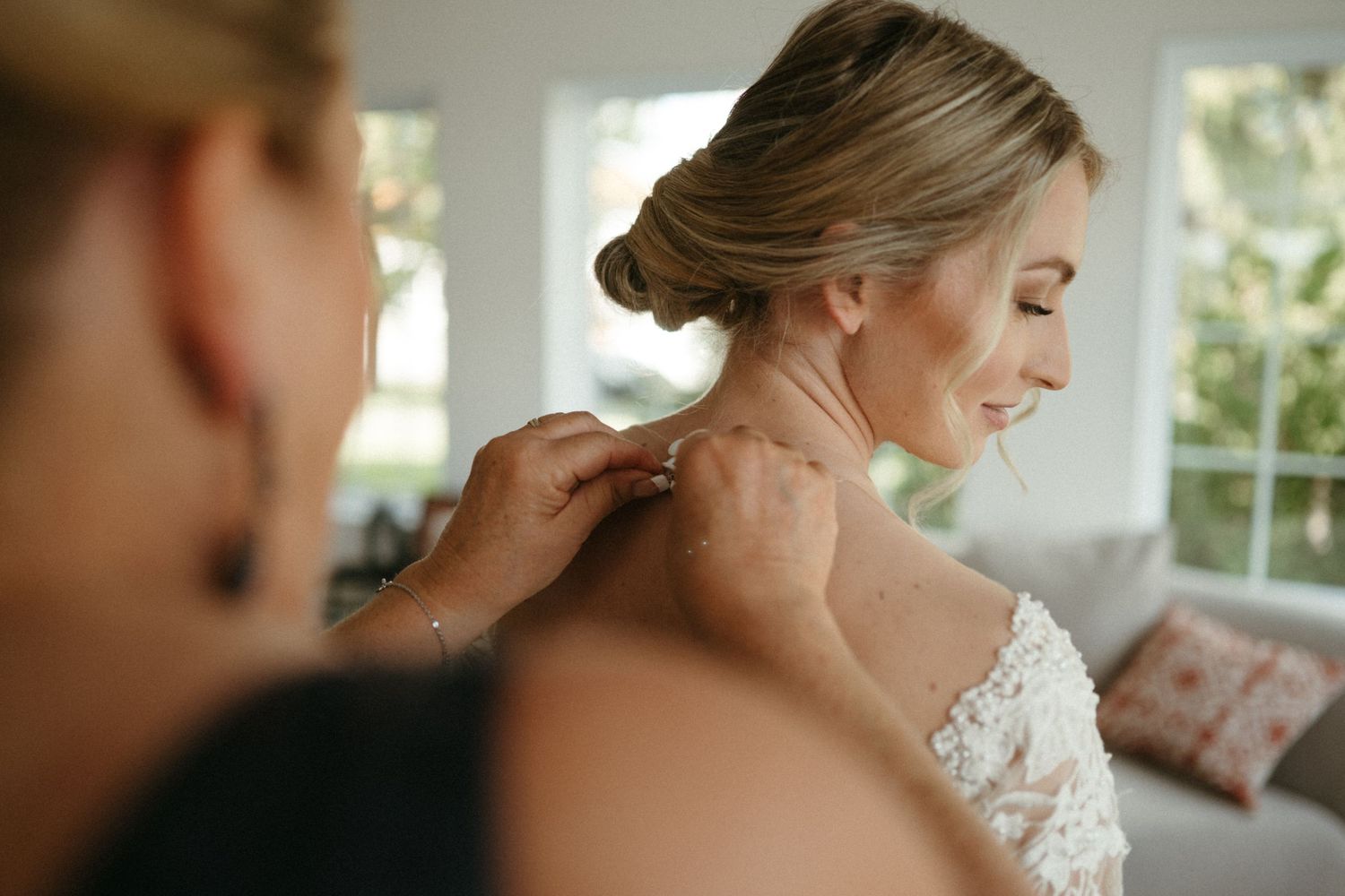 A woman with an elegant updo hairstyle is being assisted by someone as she prepares for an event.