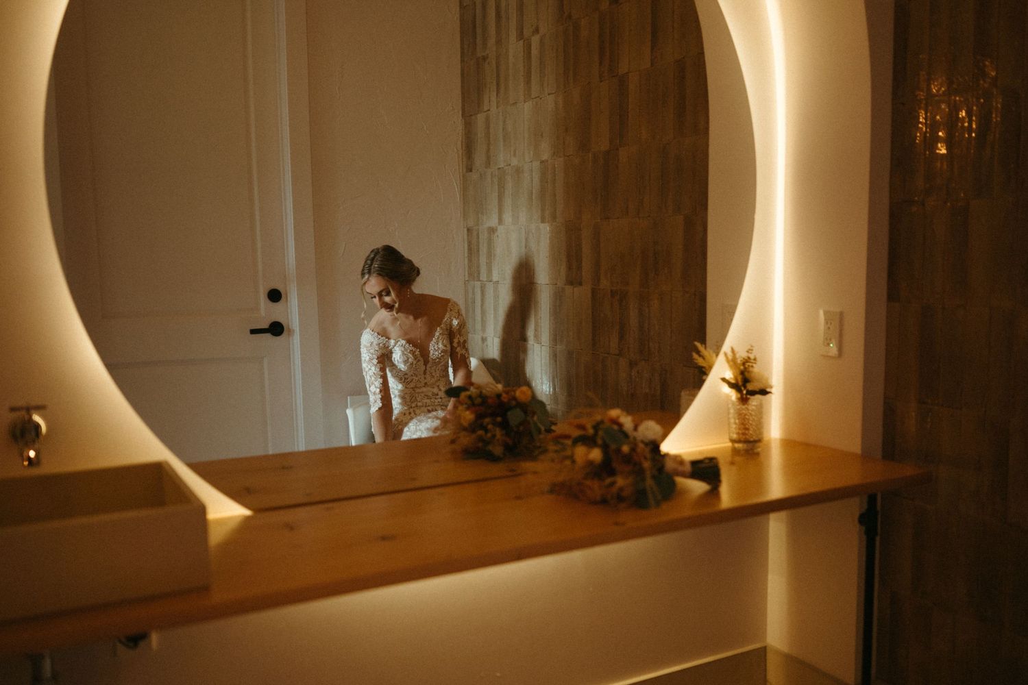 A woman stands in front of a mirror, surrounded by decorative elements, in a warm, intimate setting.