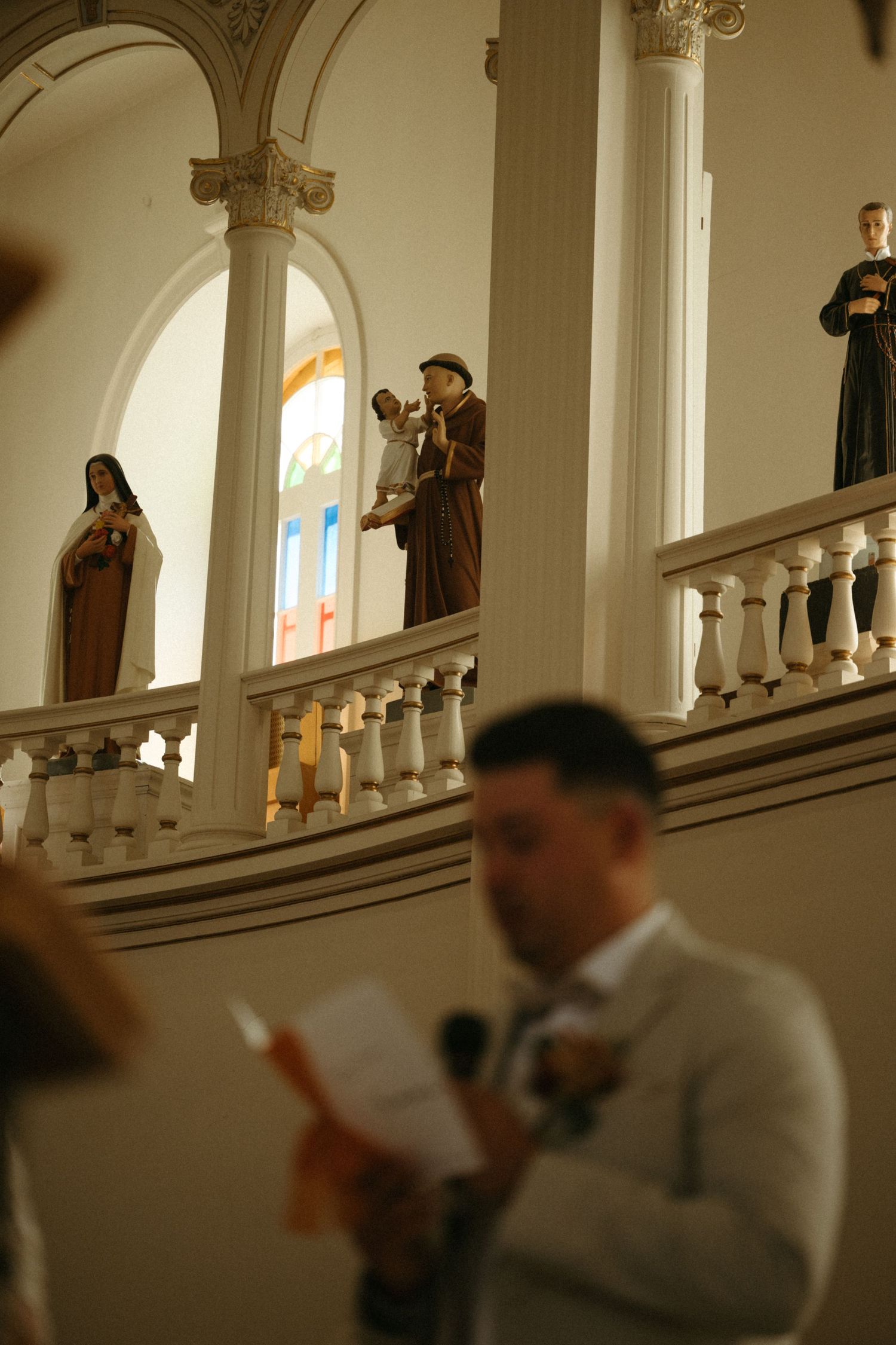 The image depicts a religious ceremony taking place in an ornate church interior, with several people visible on a balcony.