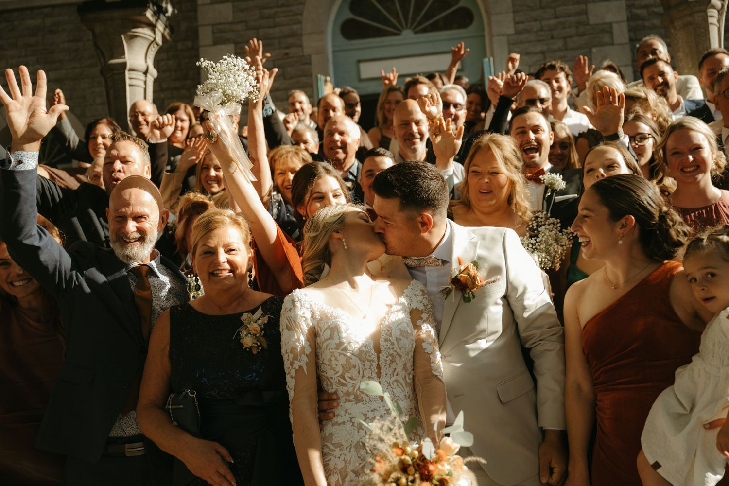 A large crowd of people, some in wedding attire, gathered outside of a building.
