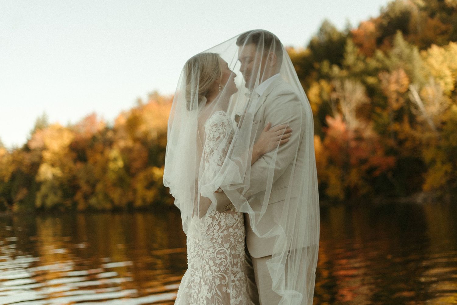 A bride and groom embracing each other in a scenic outdoor setting with fall foliage in the background.