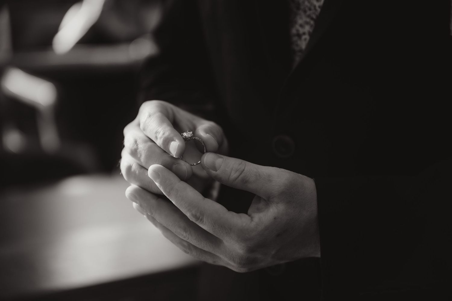 Black and white close-up of clasped hands holding a wedding ring.