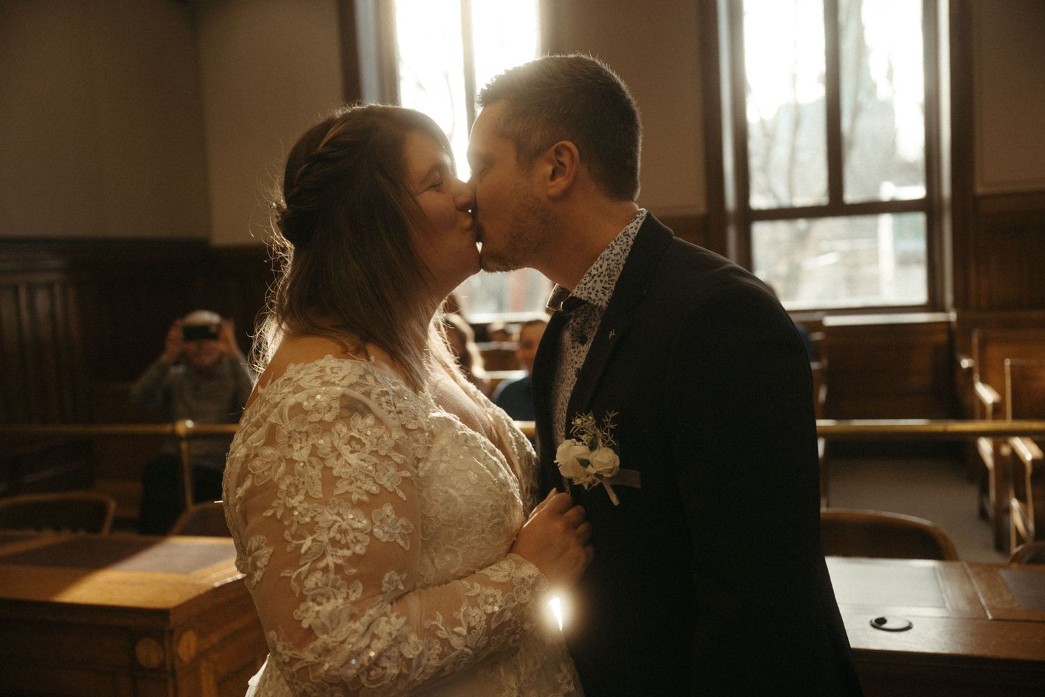 Bride and groom share a romantic kiss during their wedding ceremony in a warmly lit historic venue.