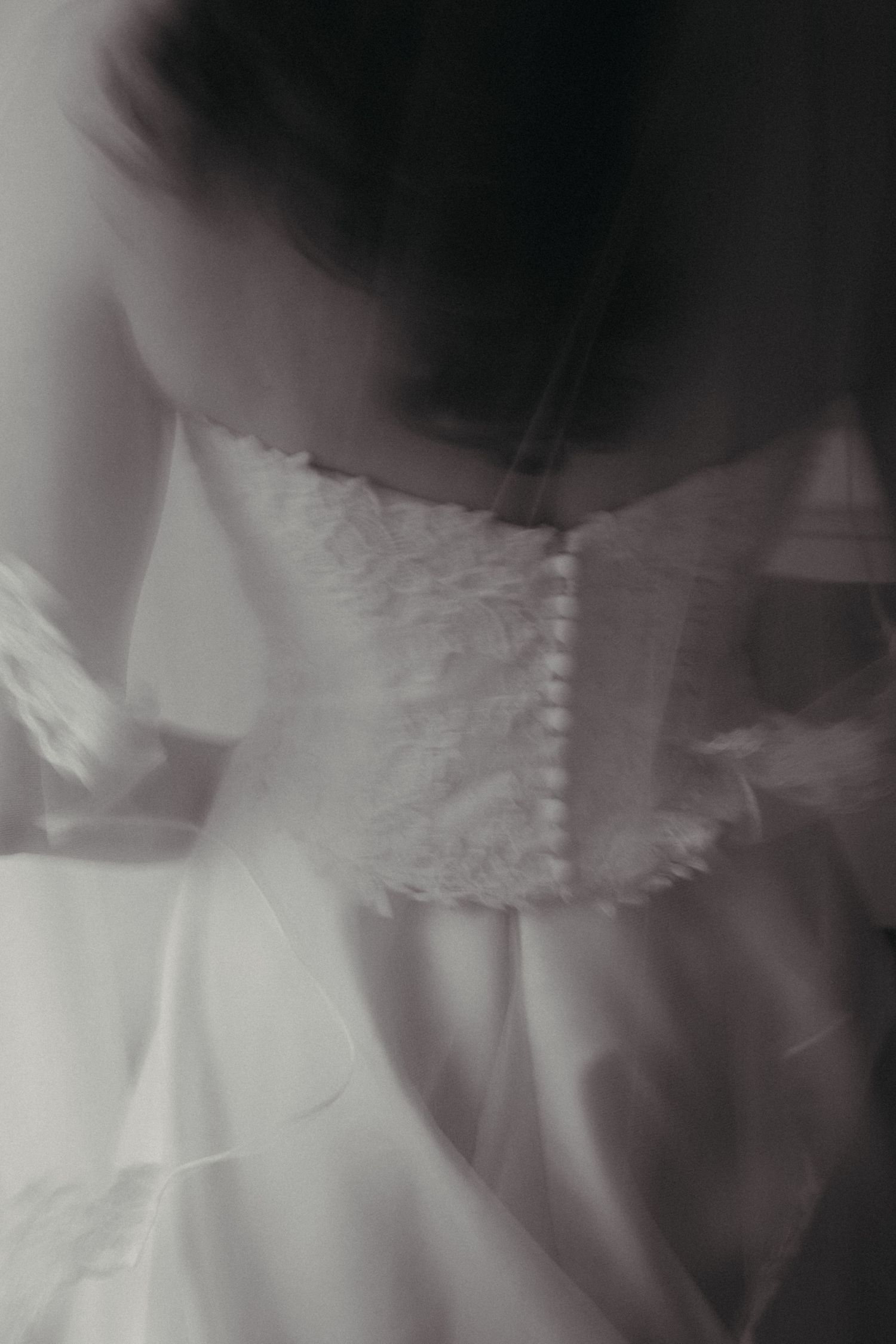 Black and white close-up of a bridal gown back with delicate lace buttons and flowing fabric.